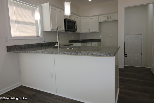 kitchen with kitchen peninsula, decorative light fixtures, dark wood-type flooring, white cabinetry, and dark stone countertops