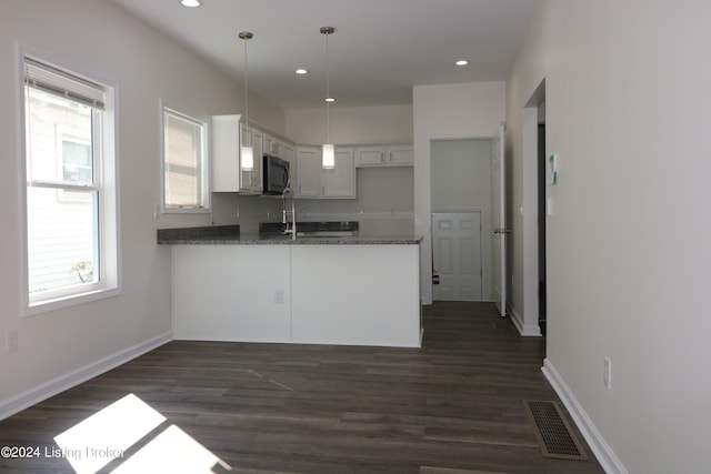 kitchen with hanging light fixtures, dark stone countertops, white cabinetry, kitchen peninsula, and dark hardwood / wood-style floors