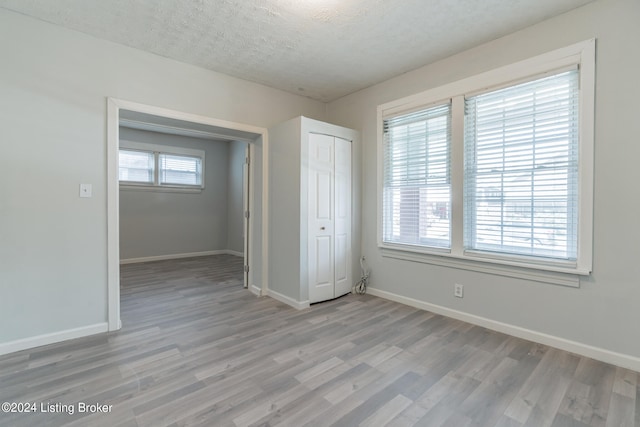 unfurnished bedroom featuring a textured ceiling, light hardwood / wood-style flooring, and multiple windows