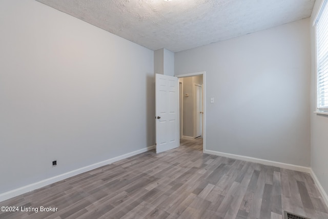 empty room with light wood-type flooring and a textured ceiling