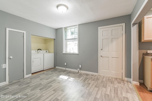 clothes washing area with a textured ceiling, washing machine and dryer, and light hardwood / wood-style flooring