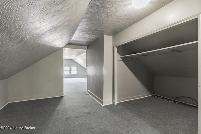 additional living space featuring a textured ceiling, vaulted ceiling, and dark colored carpet