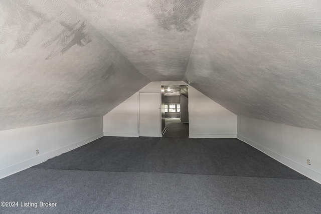 additional living space with a textured ceiling, vaulted ceiling, and dark colored carpet