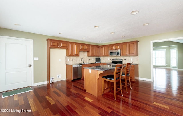 kitchen featuring appliances with stainless steel finishes, dark hardwood / wood-style flooring, a kitchen island, and dark stone countertops