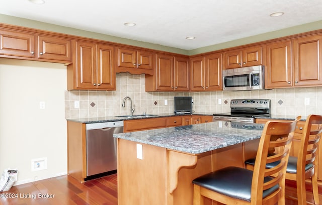 kitchen featuring stainless steel appliances, tasteful backsplash, light stone counters, a kitchen bar, and hardwood / wood-style flooring