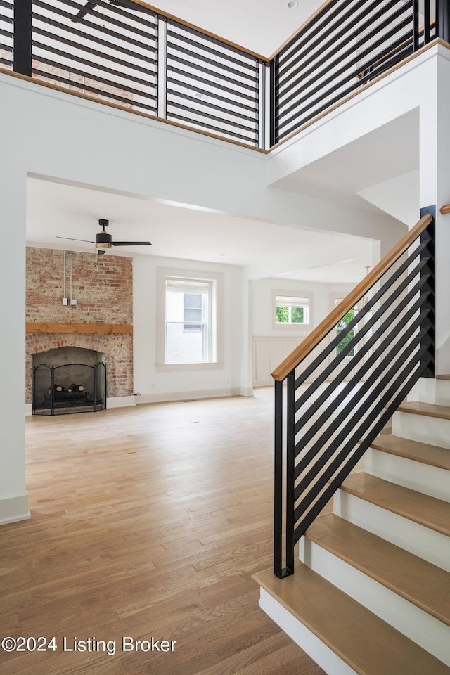 stairway featuring a high ceiling, hardwood / wood-style floors, a large fireplace, and a healthy amount of sunlight