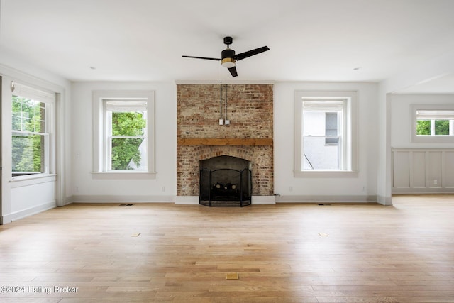 unfurnished living room featuring light hardwood / wood-style floors, ceiling fan, a brick fireplace, and plenty of natural light