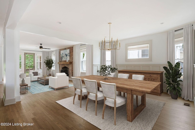 dining room featuring wood-type flooring, ceiling fan with notable chandelier, a fireplace, and a healthy amount of sunlight