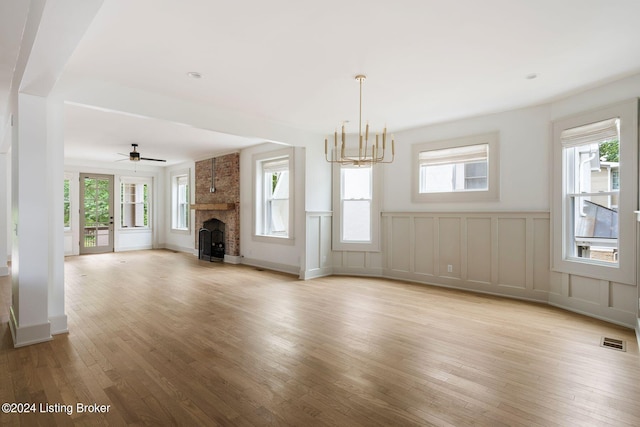 unfurnished living room with ceiling fan with notable chandelier, light hardwood / wood-style floors, plenty of natural light, and a fireplace