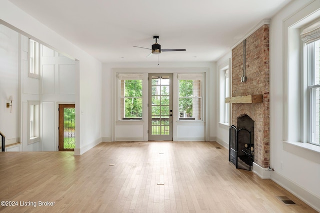 unfurnished living room featuring light wood-type flooring, ceiling fan, and a stone fireplace