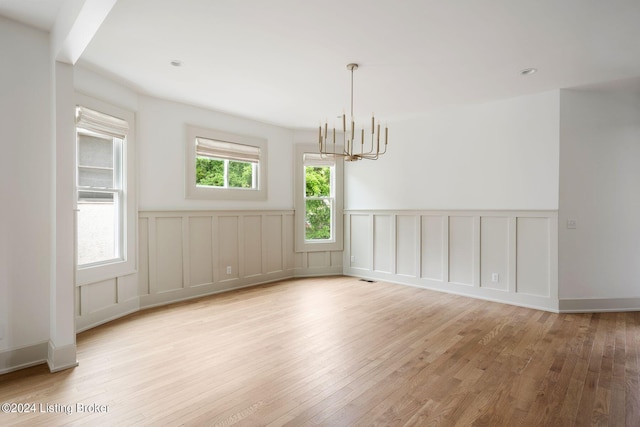 unfurnished room featuring an inviting chandelier, light hardwood / wood-style flooring, and a wealth of natural light