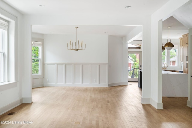 empty room featuring a notable chandelier, plenty of natural light, and light hardwood / wood-style floors