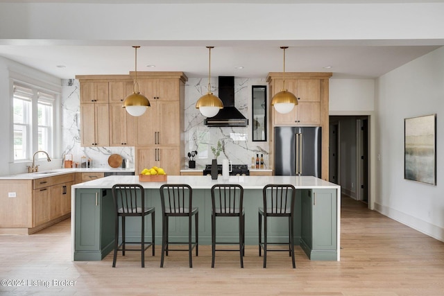 kitchen with hanging light fixtures, a kitchen island, light wood-type flooring, high quality fridge, and wall chimney range hood