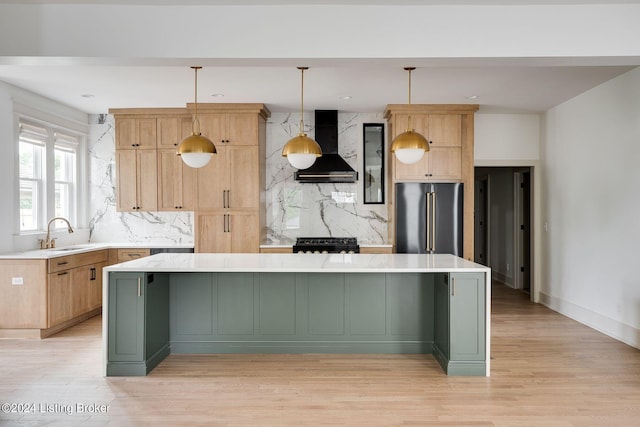 kitchen with pendant lighting, gas stove, a center island, wall chimney exhaust hood, and high end fridge