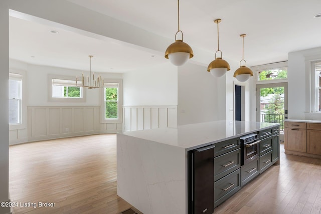 kitchen featuring pendant lighting, light wood-type flooring, light stone counters, a kitchen island, and an inviting chandelier