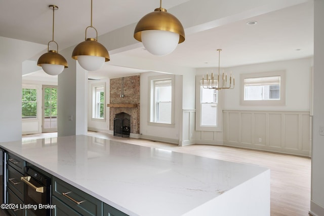 kitchen featuring a fireplace, light stone countertops, pendant lighting, a center island, and light hardwood / wood-style flooring