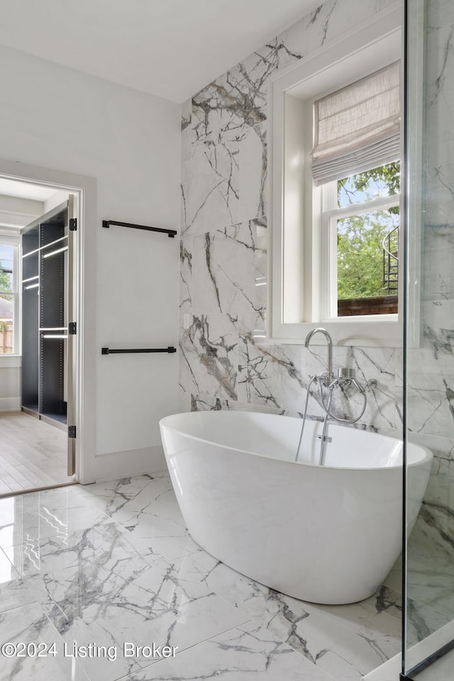 bathroom featuring a bathtub, tile walls, and a healthy amount of sunlight