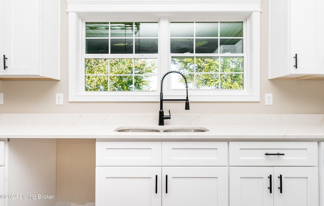 kitchen with light stone counters, sink, and white cabinets