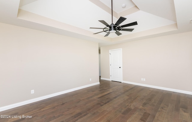 unfurnished room featuring a raised ceiling, ceiling fan, and dark wood-type flooring