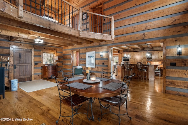 dining room with hardwood / wood-style floors, wood walls, a towering ceiling, and beamed ceiling