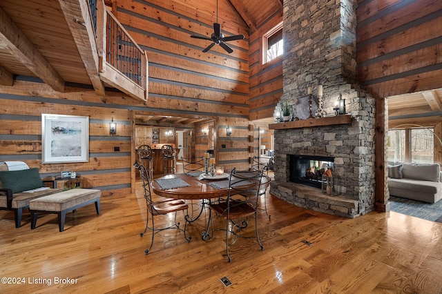 unfurnished dining area with wooden ceiling, a stone fireplace, high vaulted ceiling, wood walls, and hardwood / wood-style floors