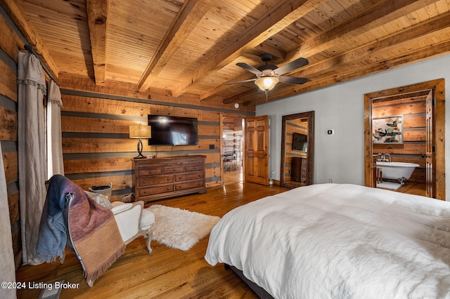 bedroom featuring beamed ceiling, wood-type flooring, connected bathroom, and wooden walls