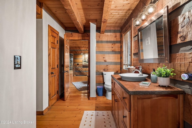 bathroom with vanity, wood walls, hardwood / wood-style flooring, toilet, and beamed ceiling