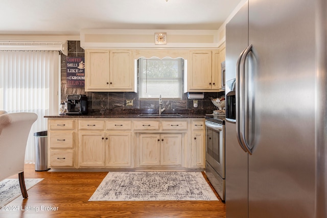 kitchen with dark stone counters, light hardwood / wood-style floors, sink, decorative backsplash, and stainless steel appliances