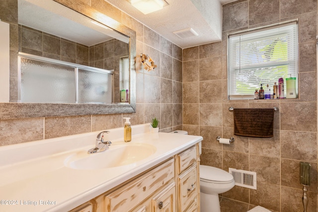 bathroom featuring tile walls, a textured ceiling, walk in shower, vanity, and toilet