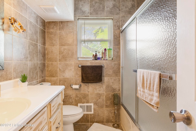 full bathroom featuring vanity, tile walls, toilet, and combined bath / shower with glass door