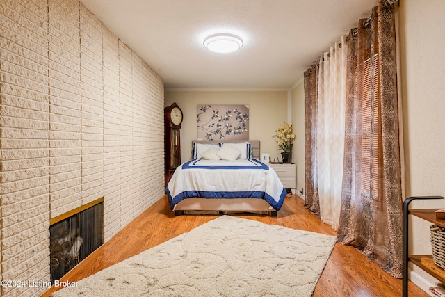 bedroom featuring brick wall, a fireplace, hardwood / wood-style floors, and crown molding