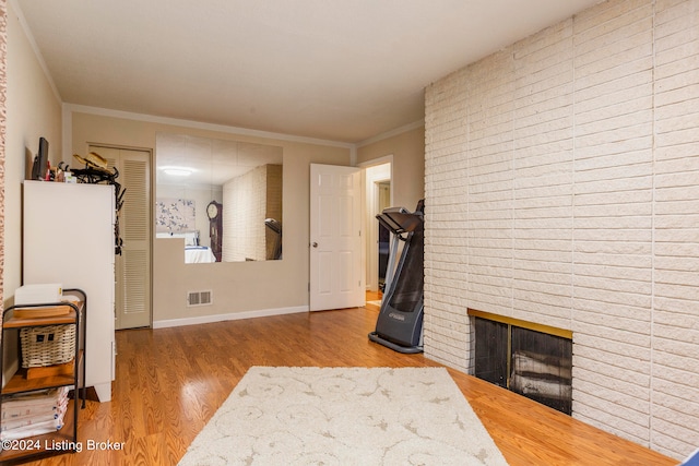 living room featuring a brick fireplace, light wood-type flooring, and ornamental molding