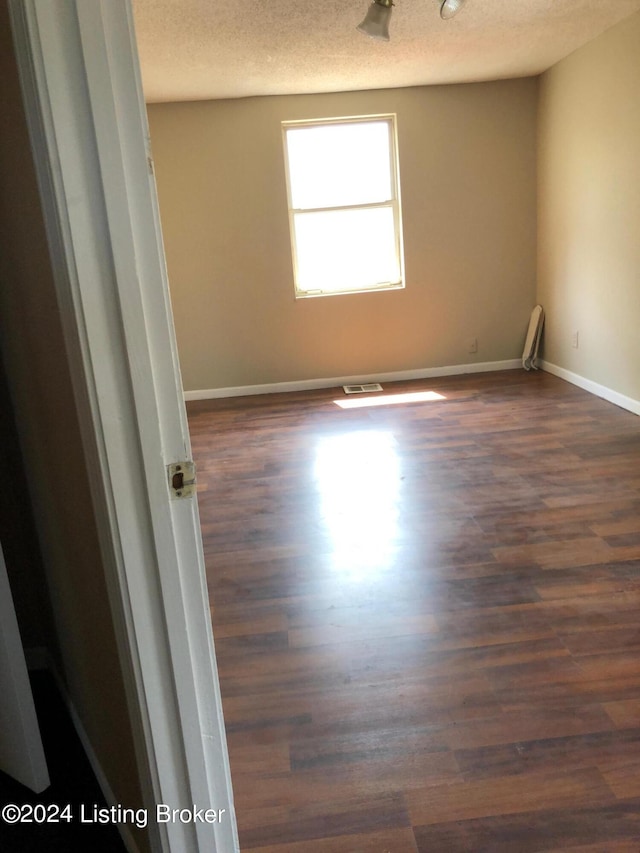 spare room featuring a textured ceiling and dark hardwood / wood-style flooring