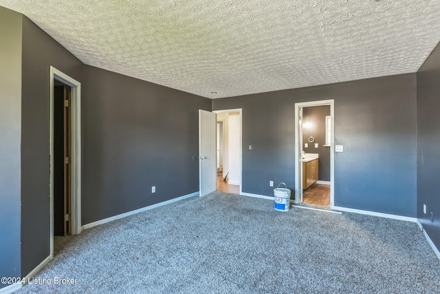 unfurnished bedroom with a textured ceiling, carpet floors, and ensuite bath