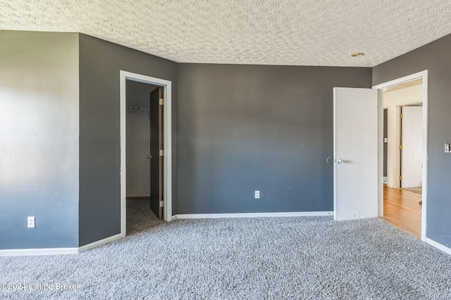 unfurnished bedroom featuring a closet, a textured ceiling, a spacious closet, and carpet flooring