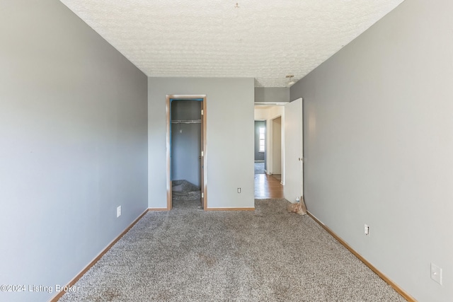 unfurnished bedroom with a textured ceiling, a walk in closet, carpet flooring, and a closet