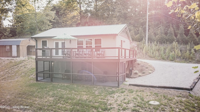 rear view of house with a deck, a lawn, and a storage unit