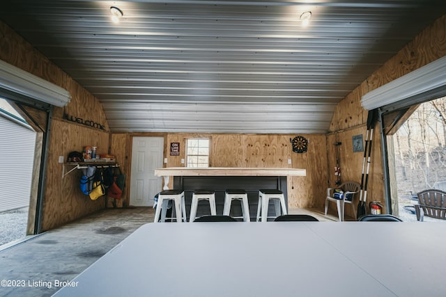 dining area featuring vaulted ceiling, concrete flooring, and wood walls