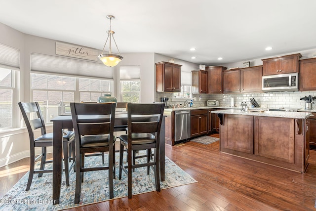 kitchen featuring a center island, stainless steel appliances, backsplash, decorative light fixtures, and dark hardwood / wood-style flooring