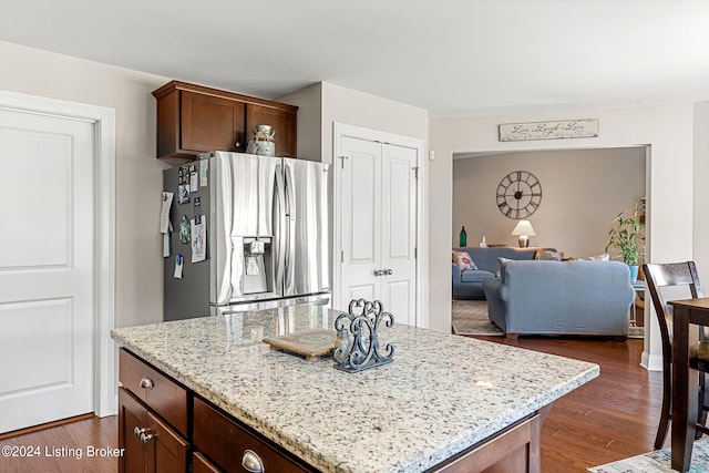 kitchen with light stone counters, a kitchen island, dark wood-type flooring, and stainless steel fridge