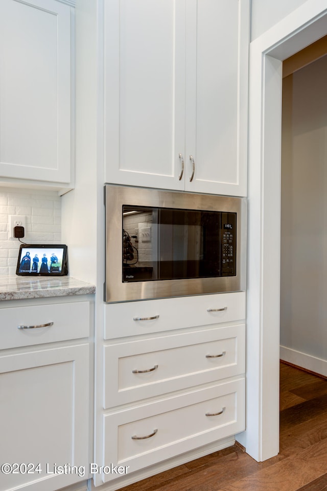 bar with wood-type flooring, light stone counters, white cabinetry, and built in microwave