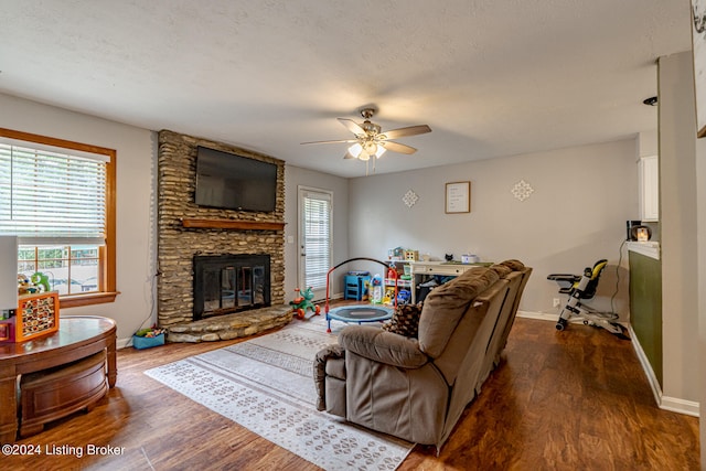 living room with a textured ceiling, a stone fireplace, dark hardwood / wood-style flooring, and ceiling fan