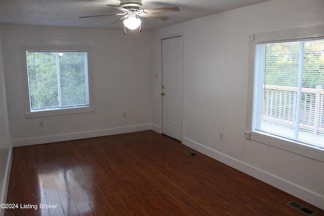 empty room with ceiling fan, a textured ceiling, dark hardwood / wood-style floors, and a wealth of natural light