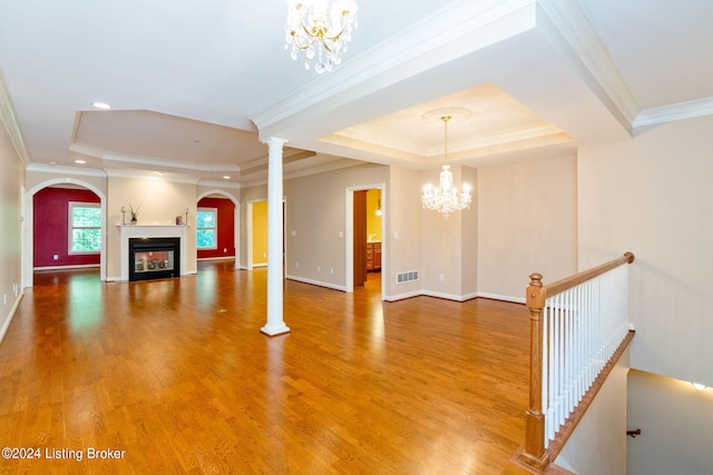 unfurnished living room with hardwood / wood-style flooring, a raised ceiling, ornamental molding, and an inviting chandelier