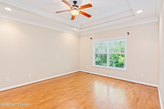 empty room featuring a raised ceiling, crown molding, light hardwood / wood-style flooring, and ceiling fan