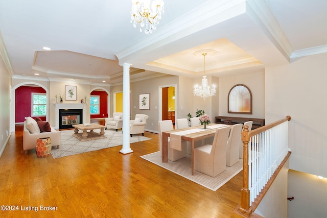 dining room with a multi sided fireplace, a notable chandelier, crown molding, wood-type flooring, and a tray ceiling