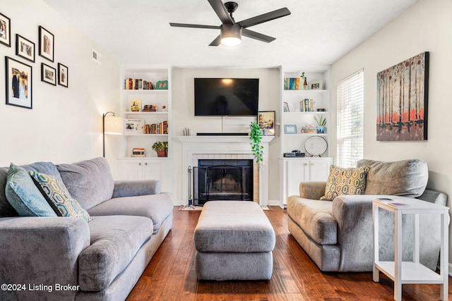 living room with built in features, ceiling fan, a tile fireplace, and dark hardwood / wood-style flooring