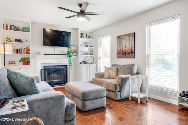 living room featuring wood-type flooring, ceiling fan, a tile fireplace, and a healthy amount of sunlight