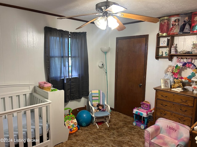 bedroom with carpet flooring, ceiling fan, a textured ceiling, a nursery area, and ornamental molding