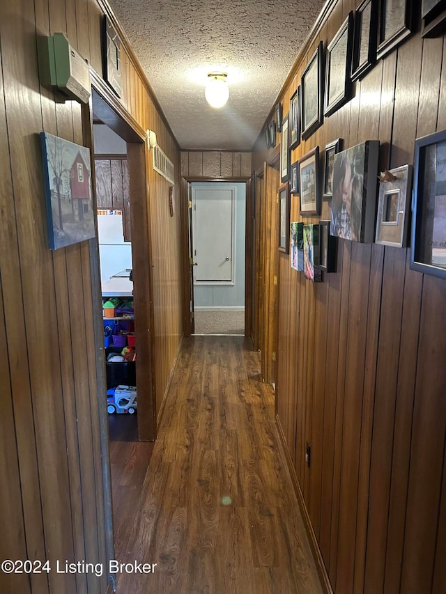 hallway featuring a textured ceiling, dark hardwood / wood-style floors, and wooden walls